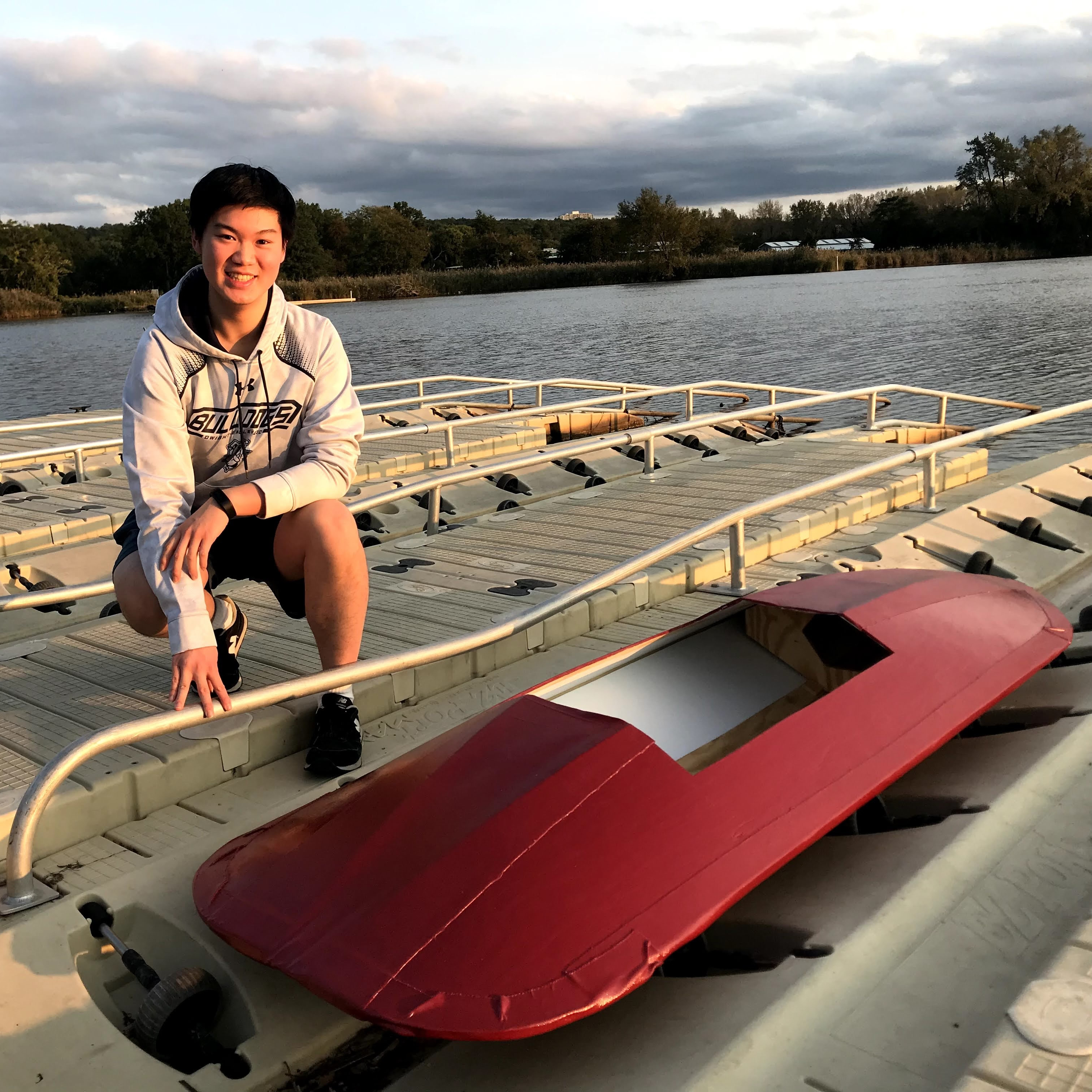 Kenneth kneeling on a dock next to a homemade kayak.